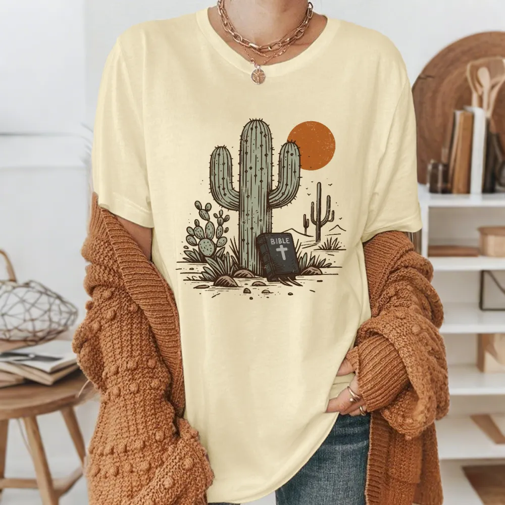 Cactus, With Small Cacti Next To It And A Tombstone With A Cross, With A Cactus Outline And An Orange Circular Sun Western Pattern In The Distance, Casual T-Shirt.