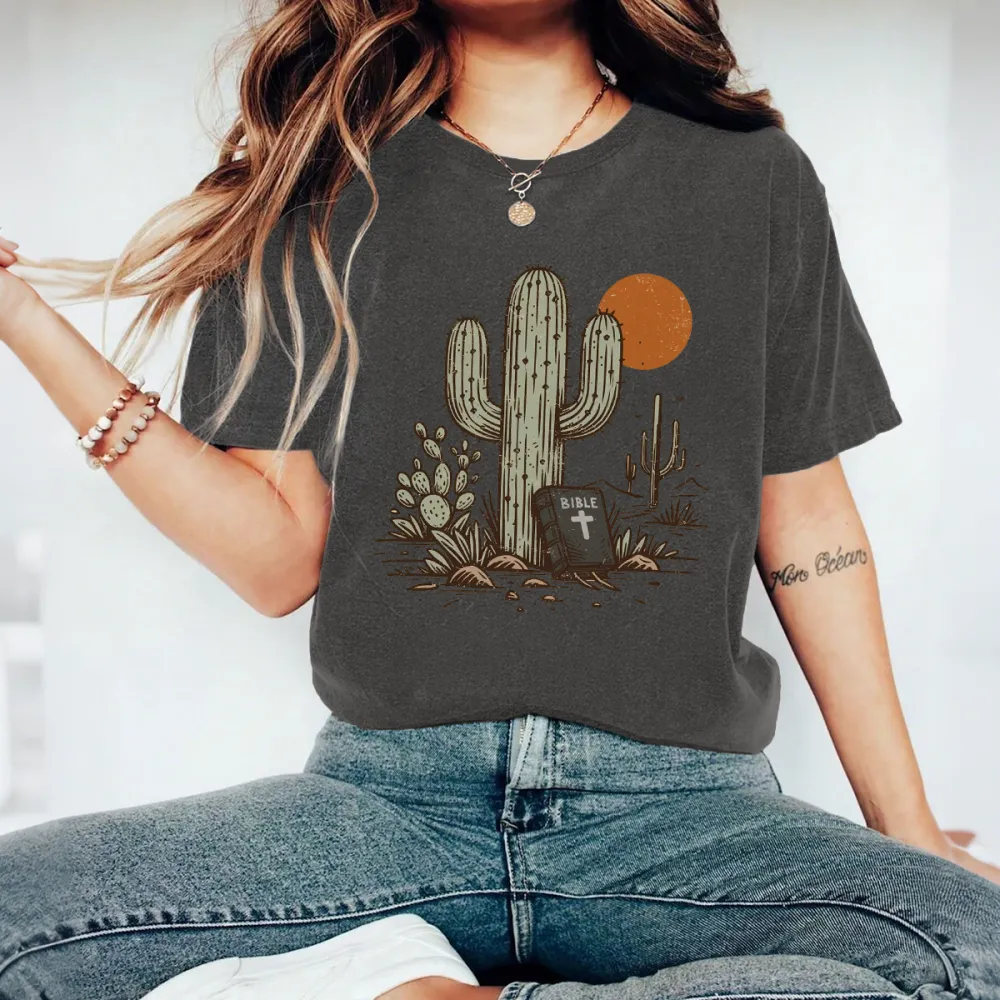 Cactus, With Small Cacti Next To It And A Tombstone With A Cross, With A Cactus Outline And An Orange Circular Sun Western Pattern In The Distance, Casual T-Shirt.